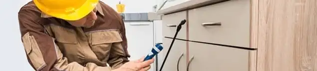 Roach exterminator applying treatment under kitchen cabinets in Sterling Heights, MI